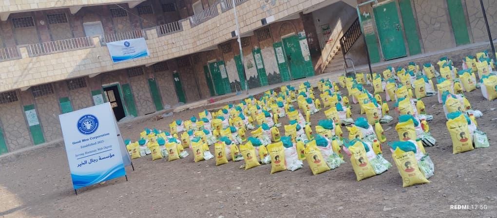 August 20, 2026 Good Men Corp distribution - Food baskets arranged beside the campaign banner at Al-Noor School